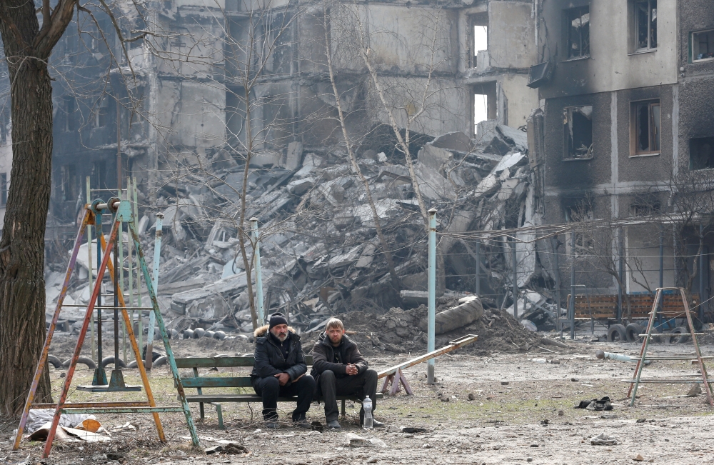 Local residents sit on a bench near an apartment building destroyed in the course of Ukraine-Russia conflict in the besieged southern port city of Mariupol, Ukraine March 25, 2022. REUTERS/Alexander Ermochenko TPX IMAGES OF THE DAY