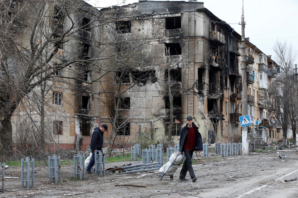 People walk past a residential building, which was heavily damaged during Ukraine-Russia conflict in the southern port city of Mariupol, Ukraine April 18, 2022. REUTERS/Alexander Ermochenko/File Photo