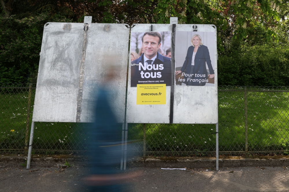 A woman walks past official campaign posters of French presidential election candidates Marine le Pen, leader of French far-right National Rally (Rassemblement National) party , and French President Emmanuel Macron, candidate for his re-election, displayed on an official billboard in Cambrai, France, April 19, 2022. REUTERS/Pascal Rossignol