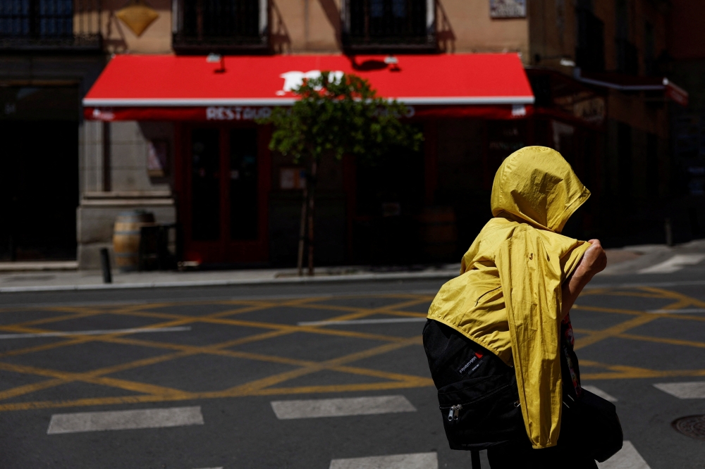 A tourist shelters from the sun underneath a jacket during the second heatwave of the year in Madrid, Spain, July 10, 2022. (REUTERS/Susana Vera)
