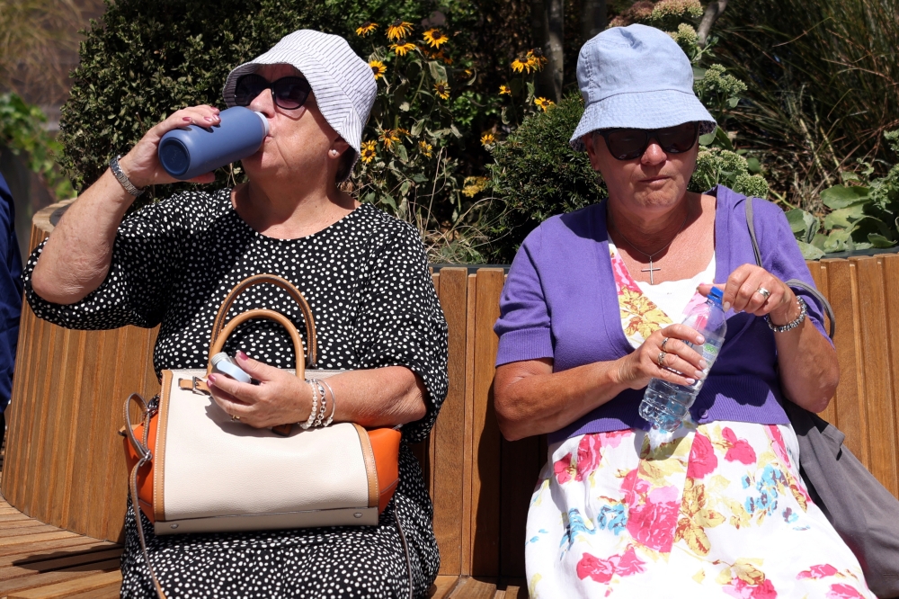 Women rest on a bench and drink water in hot weather during lunch hour in the financial district of Canary Wharf in London, Britain, July 15, 2022. (REUTERS/Kevin Coombs)