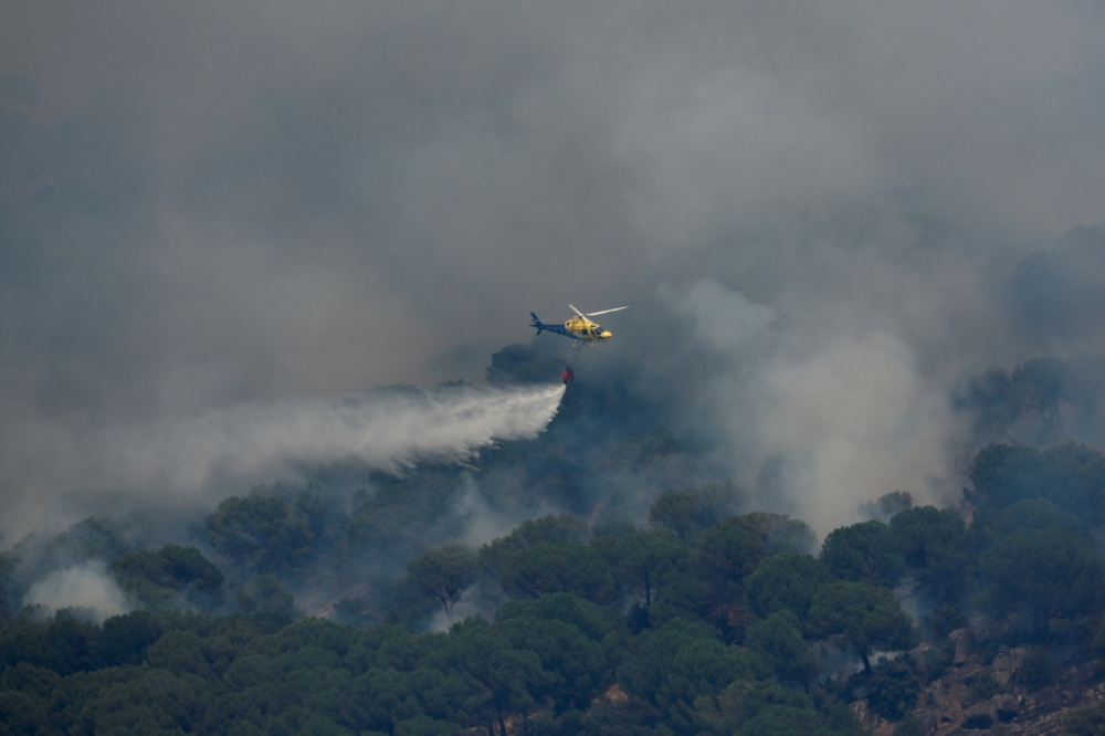 A helicopter throws water over a wildfire, as the country experiences a heatwave, in Cebreros, Avila, Spain, July 20, 2022. (REUTERS/Borja Suarez)