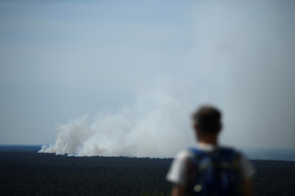 A man watches as smoke rises up above the Grunewald forest due to an explosion in a munitions depot in the Grunewald forest in Berlin, Germany August 4, 2022. REUTERS/Annegret Hilse
