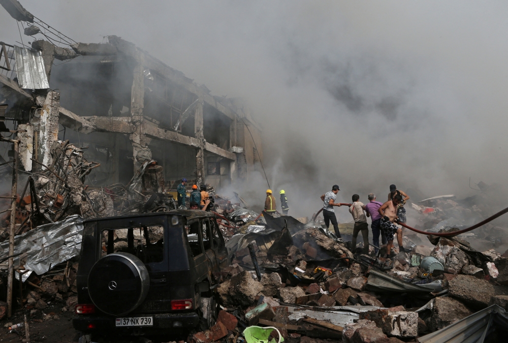 People help firefighters to extinguish a fire after blasts ripped through a fireworks warehouse in a shopping mall in Yerevan, Armenia, August 14, 2022. (Vahram Baghdasaryan/Photolure via REUTERS) 