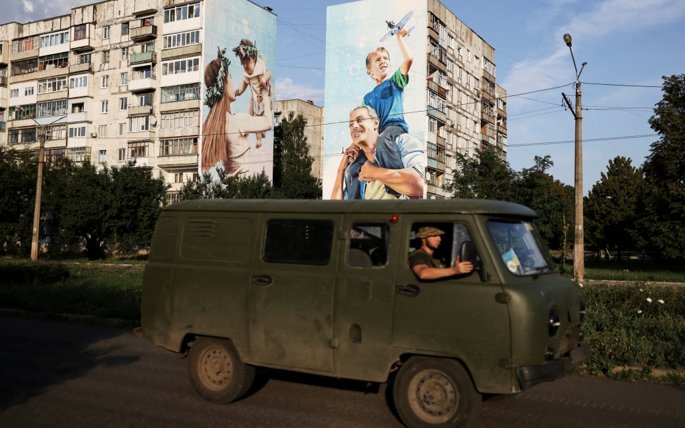 Ukraine servicemen drive past a mural of a family on damaged buildings in Bakhmut, in Donetsk region, Ukraine, August 14, 2022. (REUTERS/Nacho Doce)