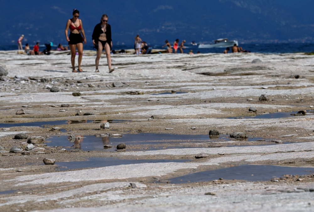 People walk as underwater rocks emerge from the water of Lake Garda after northern Italy experienced the worst drought in 70 years in Sirmione, Italy, on August 16, 2022. File Photo / Reuters
