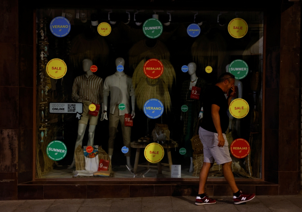 A man walks past mannequins displayed in the window of a store with the lights off to comply with the Spanish government's measures to save energy, in Ronda, Spain, August 25, 2022. (REUTERS/Jon Nazca)