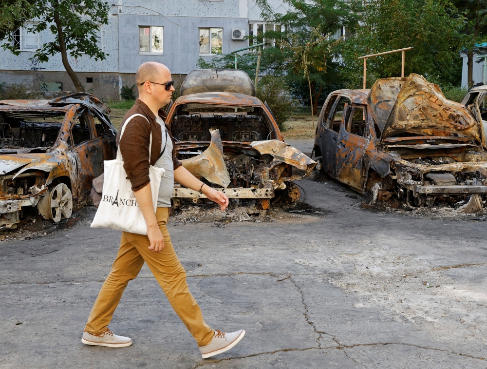 A local resident walks past cars destroyed by recent shelling in the course of Ukraine-Russia conflict in the Russian-controlled city of Enerhodar in Zaporizhzhia region, Ukraine, on August 30, 2022.  REUTERS/Alexander Ermochenko