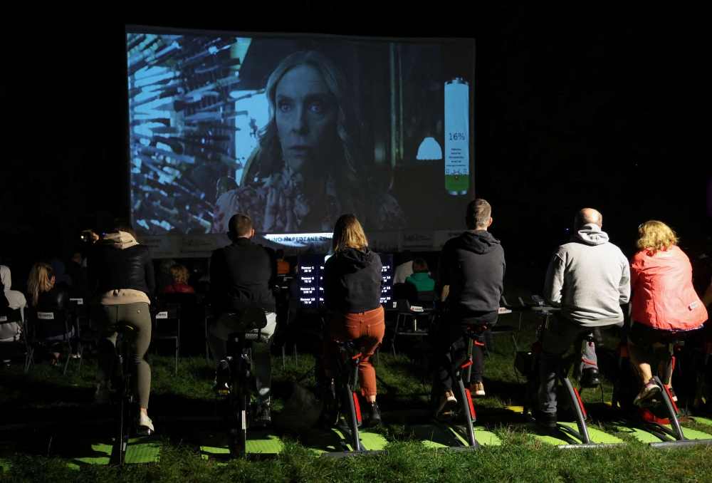People pedal stationary bikes and generate up to 50% of the energy at a pop-up outdoor cinema in a park in Warsaw, Poland September 2, 2022. Reuters/Kacper Pempel