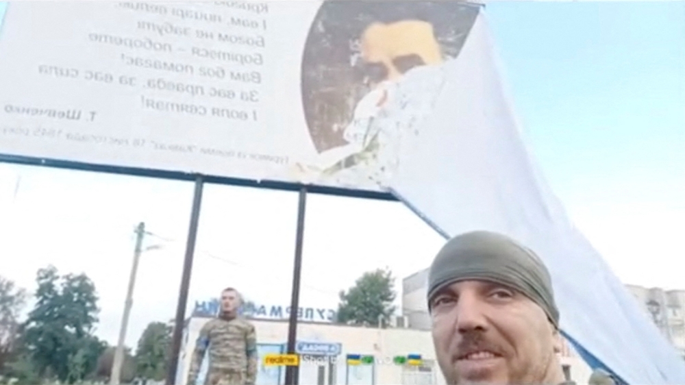 Ukrainian servicemen pull a Russian poster off a billboard, revealing a poem by Taras Shevchenko, following Russia's invasion, in Balakliia, Kharkiv Region, Ukraine, in this screen grab taken from a video obtained by REUTERS released on September 10, 2022. Video obtained by REUTERS 
