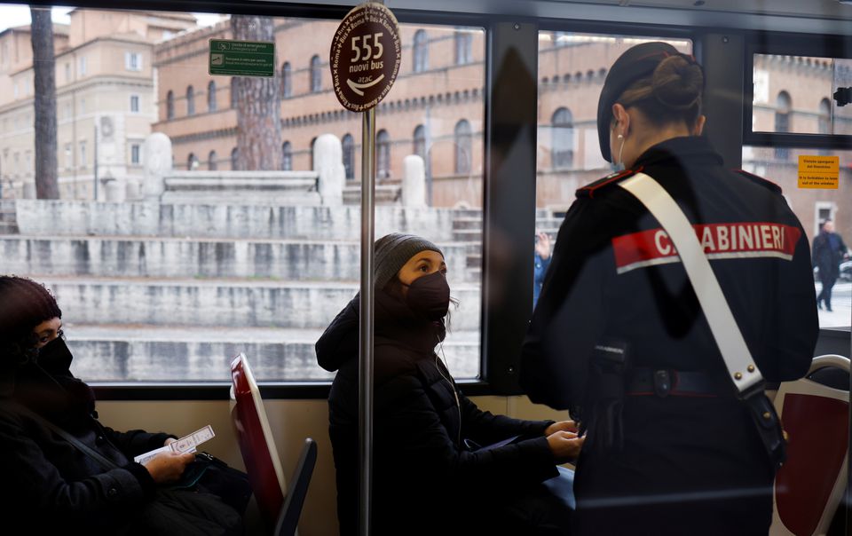 A Carabiniere checks a passenger's coronavirus disease (COVID-19) health pass, known as a Green Pass, aboard a bus the day the government restricts access of unvaccinated to indoor venues, in Rome, Italy December 6, 2021. Picture taken through glass. REUTERS/Yara Nardi
