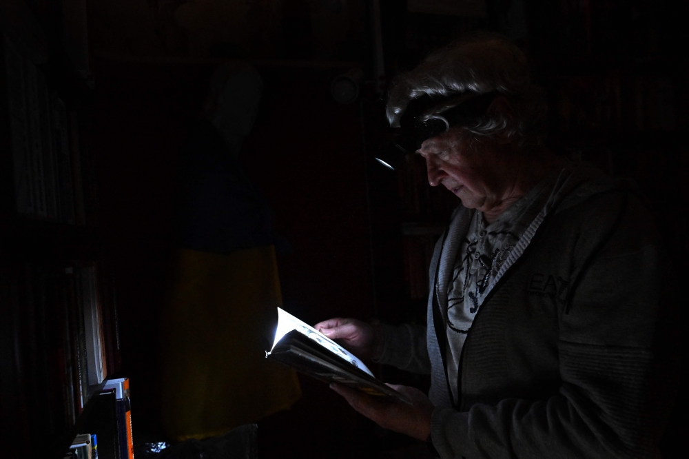 This photograph taken on November 5, 2022, shows physicist Igor Zhuk, 70-years-old, reading a book with help of his headlamp during a power cut in his building, in the north of the Ukrainian capital of Kyiv. (Photo by Sergei SUPINSKY / AFP)