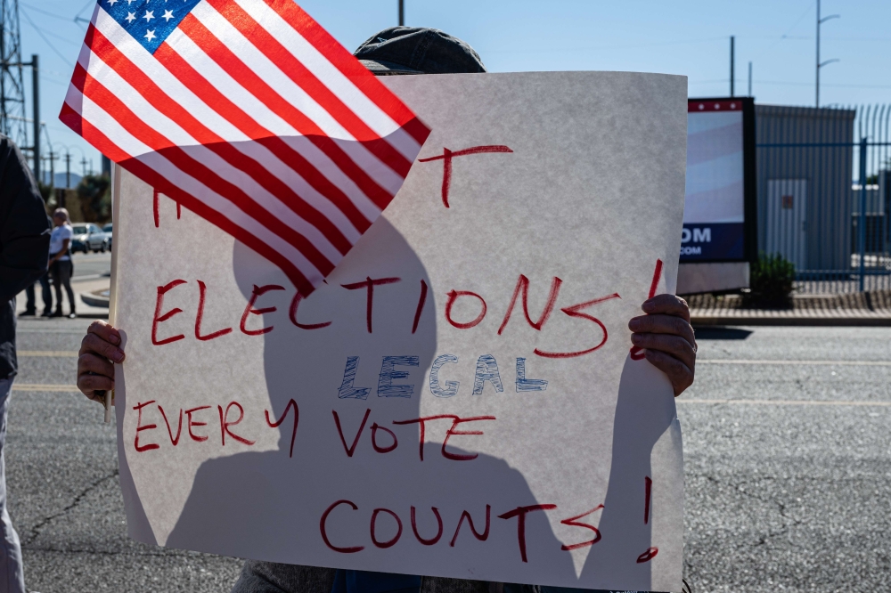 A right wing activists stands on the sidewalk with a sign in protest of the election process in front of the Maricopa County Tabulation and election Center on November 12, 2022 in Phoenix, Arizona. (AFP/Jon Cherry)