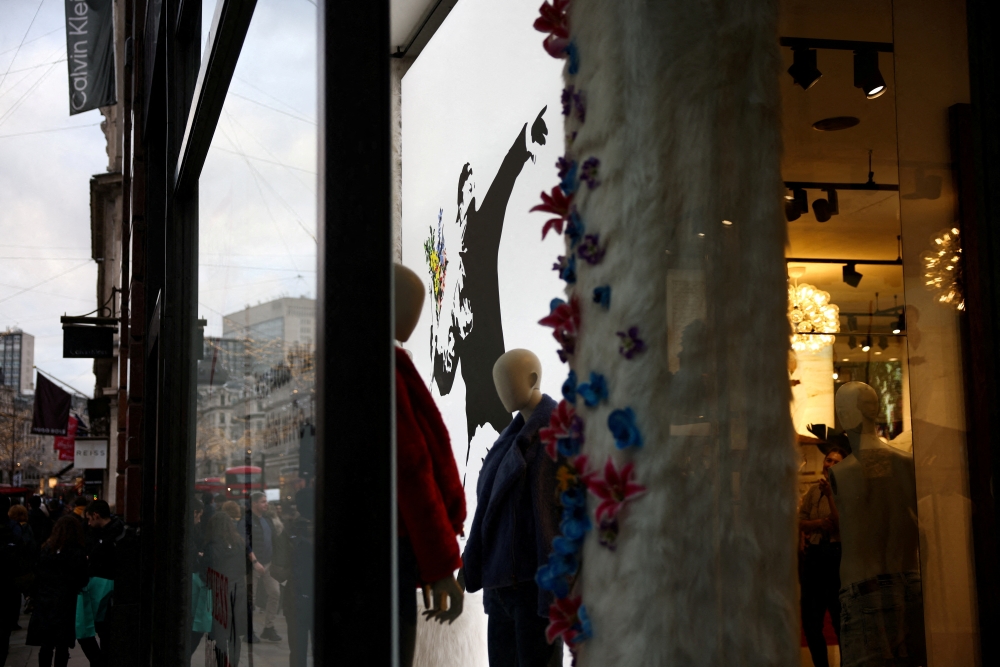 A person walks past the window display of a Guess store which includes the artwork 