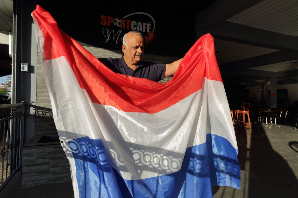 Owner of Sportscafe Munder, Ramesh Jagesar, poses for a picture while holding a flag of the Netherlands in Paramaribo, Suriname, on December 6, 2022. (Photo by Ranu Abhelakh / AFP)