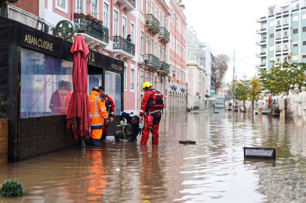 Fire fighters try to open a drain along a flooded street following heavy rains in Lisbon on December 13, 2022. (Photo by FILIPE AMORIM / AFP)