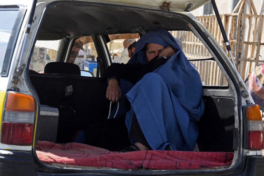 An Afghan woman sits in a parked taxi along the roadside in Kandahar on December 25, 2022. (Photo by Naveed Tanveer / AFP)