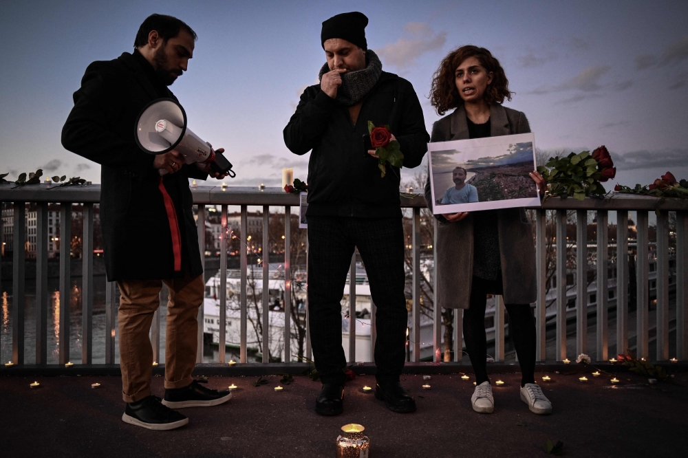 A woman holds a photographic portrait during tribute to Mohammad Moradi, an Iranian man who killed himself after jumping into the Rhone river to raise awareness about the situation of the Iranian people, in Lyon on December 27, 2022. (Photo by JEFF PACHOUD / AFP)