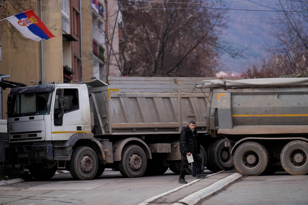 A pedestrian walks past a new road barricade set up in the divided town of Mitrovica on December 28, 2022. (Photo by Armend NIMANI / AFP)