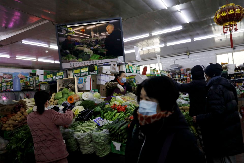 People wearing face masks following the coronavirus disease (COVID-19) outbreak shop for vegetables near an image of Beijing Communist Party Secretary Cai Qi at a market in Beijing, China January 15, 2021. Picture taken January 15, 2021. REUTERS/Tingshu Wang/File Photo
