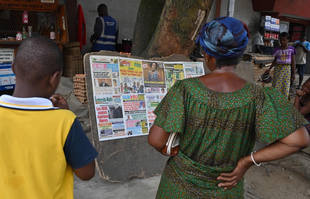 Local residents read the headlines of local newspapers after the release of 46 Ivorian soldiers arrested in July 2022 in Mali, in Abidjan on January 7, 2023.  (Photo by Issouf SANOGO / AFP)