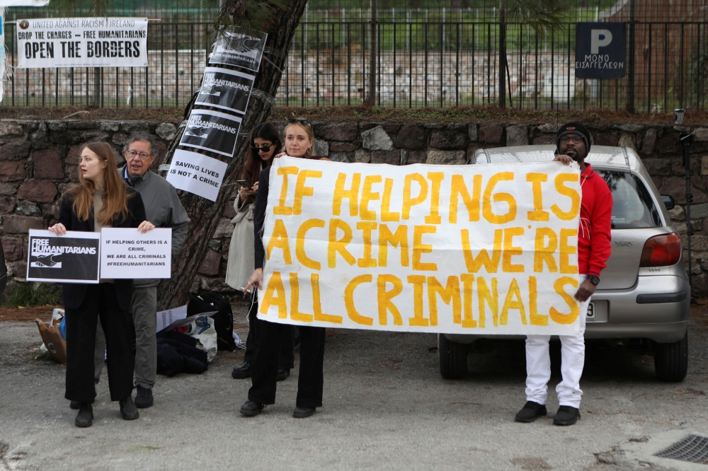 Aid worker Pieter Wittenberg, who faces trial over refugee rescues, stands next to supporters holding a banner, outside a courthouse on the island of Lesbos, Greece, January 13, 2023. (REUTERS/Elias Marcou)