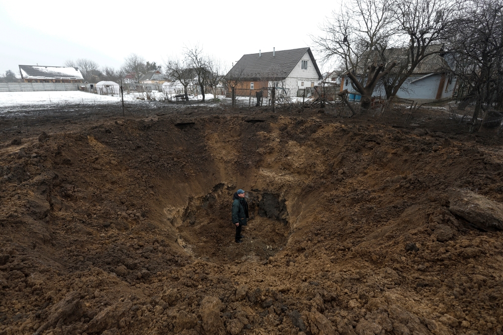 A man stands inside a crater left by a Russian missile, amid Russia's attack on Ukraine, in the village of Kopyliv, Kyiv region, Ukraine January 14, 2023. Reuters/Valentyn Ogirenko