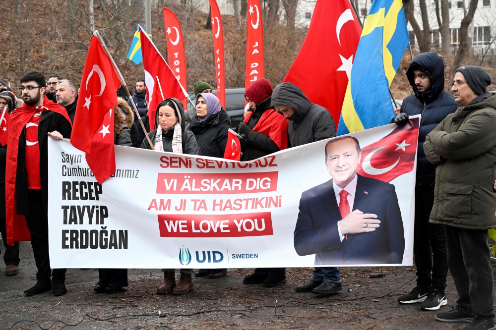 Participants hold Turkish flags and a banner reading 'Recep Tayyip Erdogan - We love you' during a demonstration of the pro-Turkish organization Union of European Turkish Democrats in support of Turkey and President Recep Tayyip Erdogan outside the Turkish Embassy in Stockholm, Sweden, on January 21, 2023.(Photo by Fredrik Sandberg / TT News Agency / AFP)