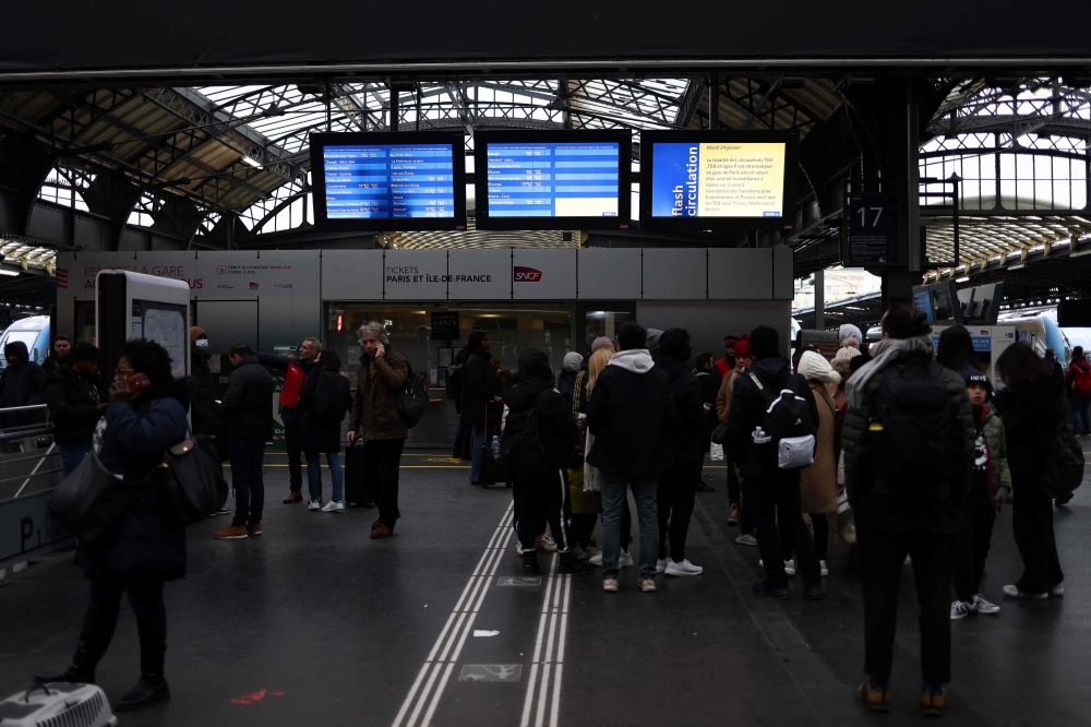 Passengers wait under screens displaying a traffic alert message during a total traffic shutdown at the Gare de l'Est train station in Paris on January 24, 2023. (Photo by Thomas Samson / AFP)