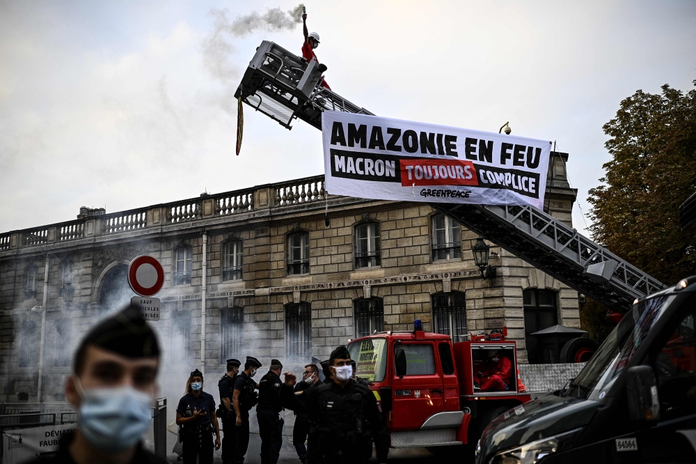 A Greenpeace activist holds a flare as he stands at the top of a fire truck ladder after activists unfolded a banner reading 'Amazon on fire Macron still complicit' in front of The Elysee Palace in Paris on September 10, 2020. (Photo by Christophe Archambault / AFP)