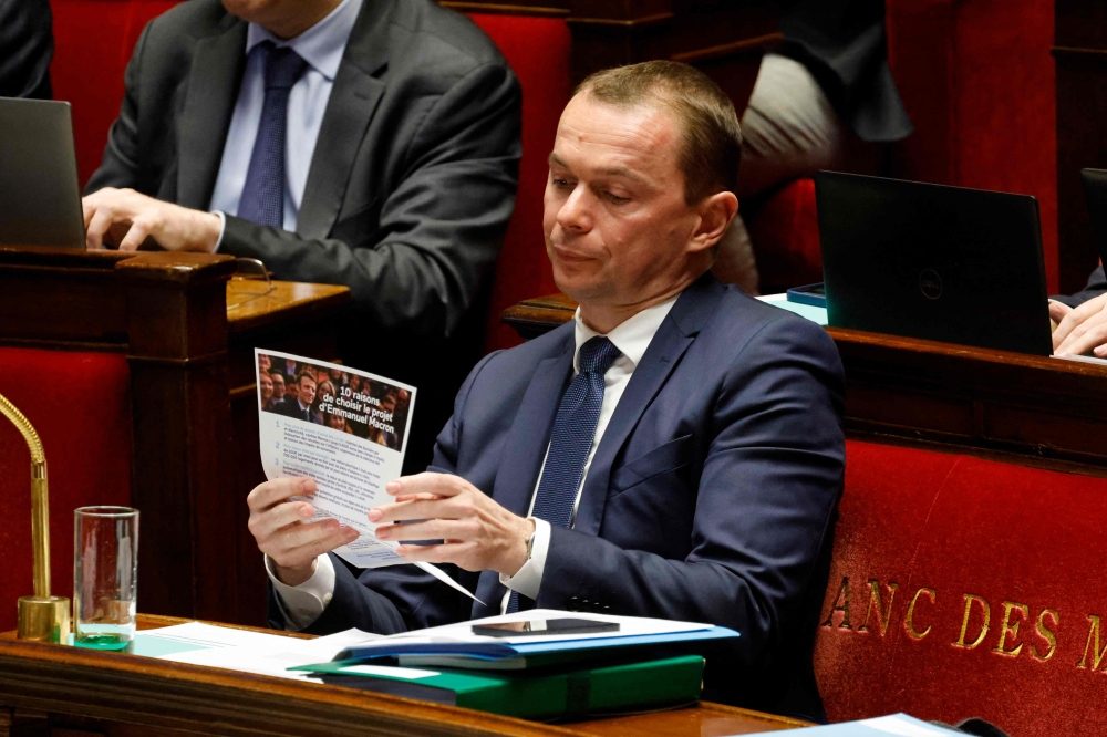 French Labour Minister Olivier Dussopt looks at a political leaflet of President Emmanuel Macron candidate for the 2022 French presidential election on pension reform during a session to discuss on the government's pension reform plan at the National Assembly, French Parliament lower house, in Paris, on February 13, 2023. (Photo by Ludovic MARIN / AFP)
