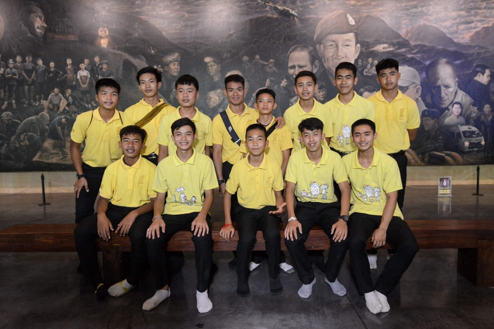 In this file photo taken on June 24, 2019 Duangpetch Promthep (front 2nd left), one of the 12 boys rescued from deep inside a Thai cave, poses for photos with other members of the 'Wild Boars' football team at the Tham Luang cave centre as they mark the first anniversary of their rescue in the Mae Sai district of Chiang Rai province. (Photo by Jittrapon Kaicome / AFP)