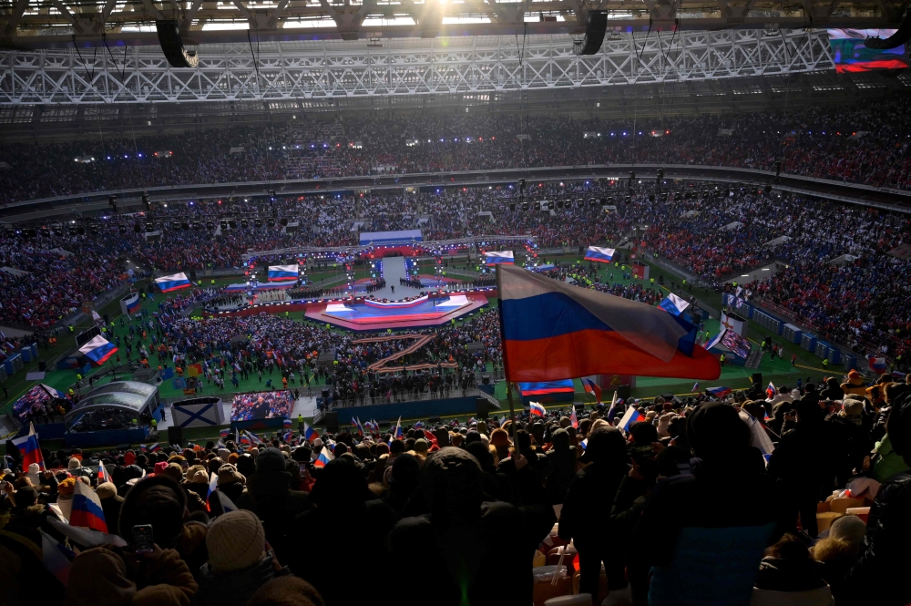 People listen as President Vladimir Putin (center on the stage) gives a speech during a patriotic concert dedicated to the upcoming Defender of the Fatherland Day at the Luzhniki stadium in Moscow on February 22, 2023. (Photo by Natalia KOLESNIKOVA / AFP)