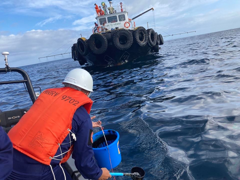In this handout photo received from the Philippine Coast Guard and taken on March 2, 2023, a coast guard personnel collects water sample from of an oil spill in the waters off Naujan, Oriental Mindoro. Photo by Handout / Philippine Coast Guard (PCG) / AFP