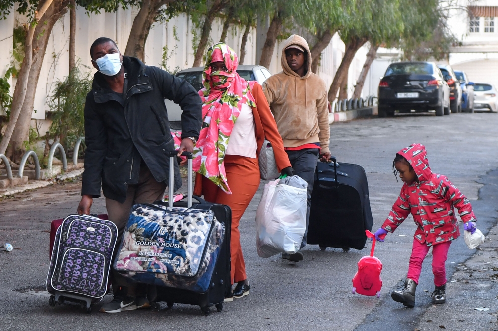 Sub-Saharan migrants head with their belongings to a bus taking them to a repatriation flight, leaving Tunis for their countries of origin. (Photo by FETHI BELAID / AFP)