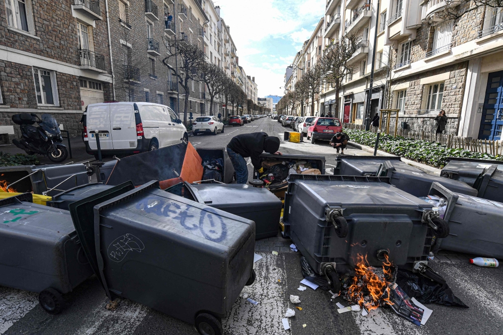 A protestor stands among rubbish bins with burning materiel during a demonstration on the eighth day of strikes and protests across the country against the government's proposed pensions overhaul, in Rennes, western France on March 15, 2023. (Photo by Jean-Francois Monier / AFP)