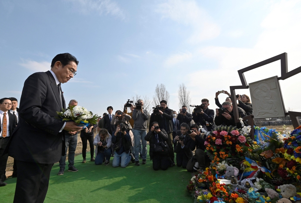 Japan's Prime Minister Fumio Kishida pays his respect at the site of a mass grave found on the grounds of the church of Saint Andrew Pervozvannoho All Saints in the town of Bucha, during a visit to Ukraine on March 21, 2023. (Photo by Sergei Chuzavkov / AFP)