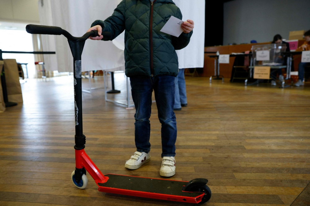 A person holds a ballot and an e-scooter during a municipal public 