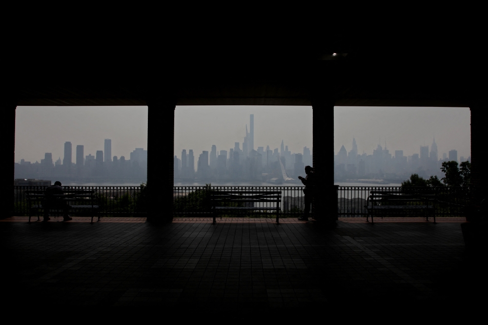 A pedestrian walks along the waterfront in West New York, New Jersey, across the Hudson River from Manhattan, as smoke haze from Canadian wildfires blankets the area. Photo by Leonardo Munoz / AFP