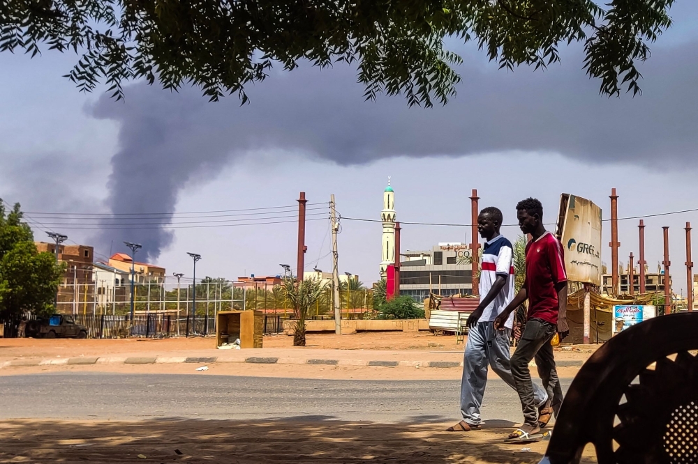 Men walk down a street in Khartoum on June 8, 2023, as smoke rises from behind buildings amid continuing fighting between the army and paramilitary forces. Photo by AFP