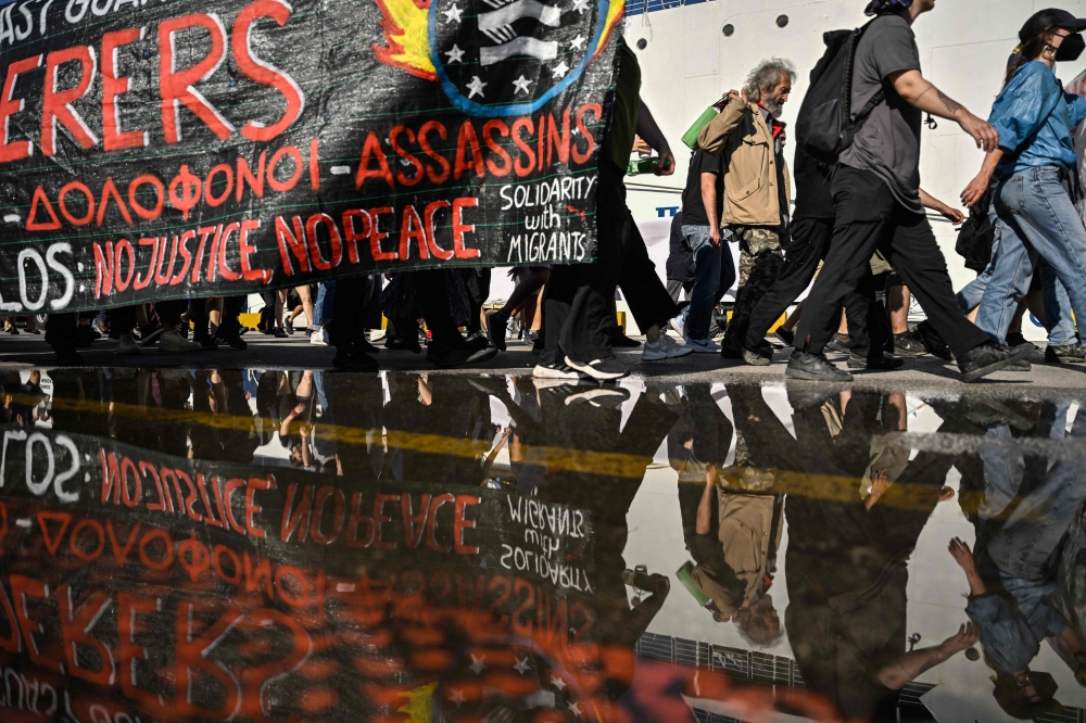 Protesters hold a banner during a protest march to the Frontex and Hellenic Coastguard headquarters in the port of Piraeus near Athens, on June 18, 2023, following the deadly shipwreck which costed lives of at least 78 migrants. (Photo by Louisa GOULIAMAKI / AFP)