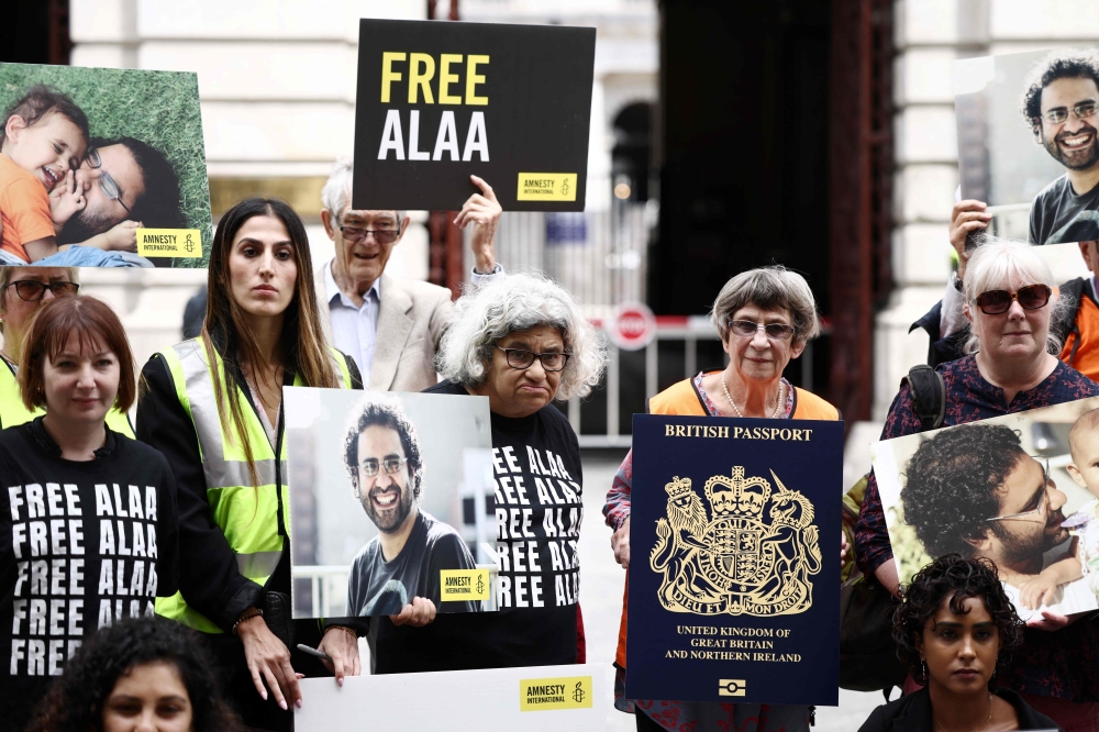 Protesters including Laila Soueif (centre), mother of jailed British-Egyptian activist Alaa Abdel Fattah, hold his pictures along with placards of British passport covers and signs reading 