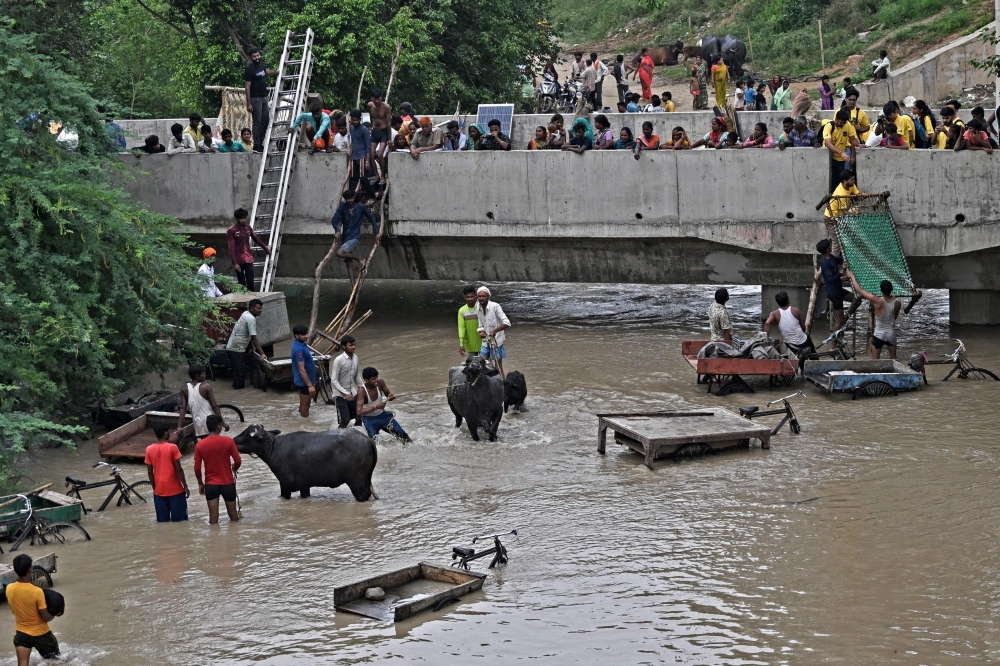 People move their belongings to safety at a bridge over the flooded Yamuna River after heavy monsoon rains in New Delhi on July 12, 2023. Photo by Arun SANKAR / AFP