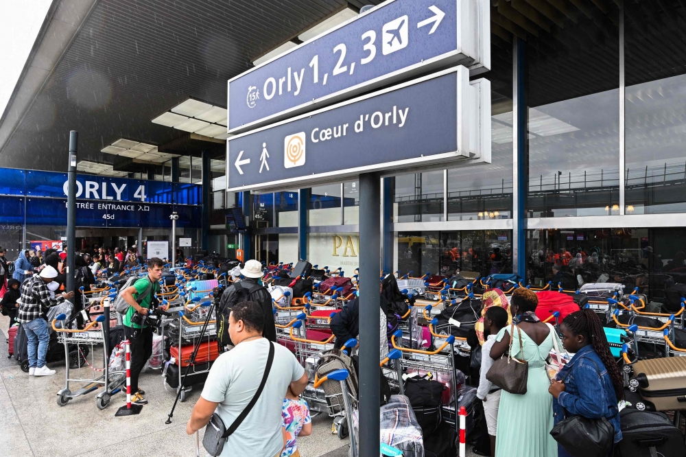 View of the entrance of the Orly 4 terminal with a sign (C) indicating the other Orly terminals and passangers waiting next to baggage carts stacked with luggage, after a technical incident at the Paris-Orly Airport, in Orly, south of Paris.