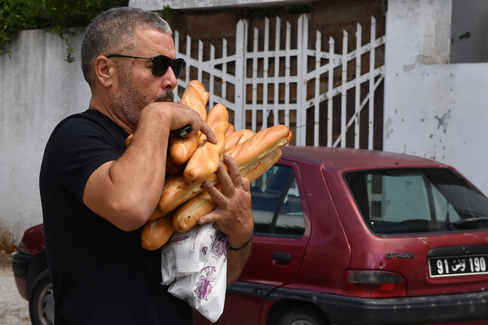 A man carries baguettes bought from a bakery in Tunis on August 7, 2023. (Photo by FETHI BELAID / AFP)
