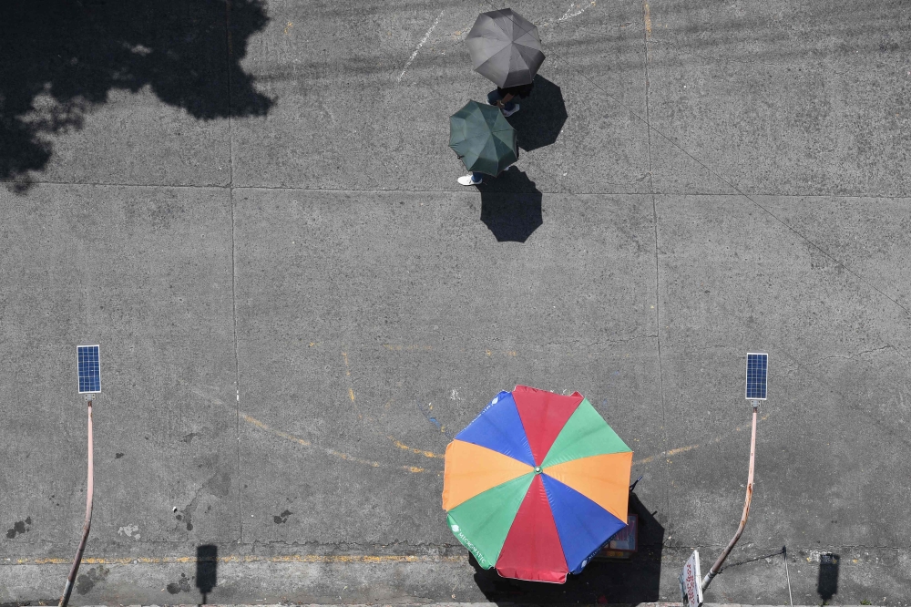 People shelter from the sun with umbrellas as they walk past a vendor in Manila on August 10, 2023. Photo by Ted ALJIBE / AFP