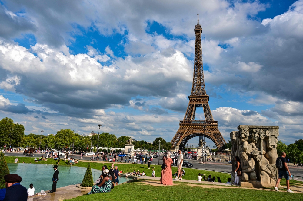 Members of the public take photographs in front of the Eiffel Tower in Paris on August 16, 2023. (Photo by MIGUEL MEDINA / AFP)