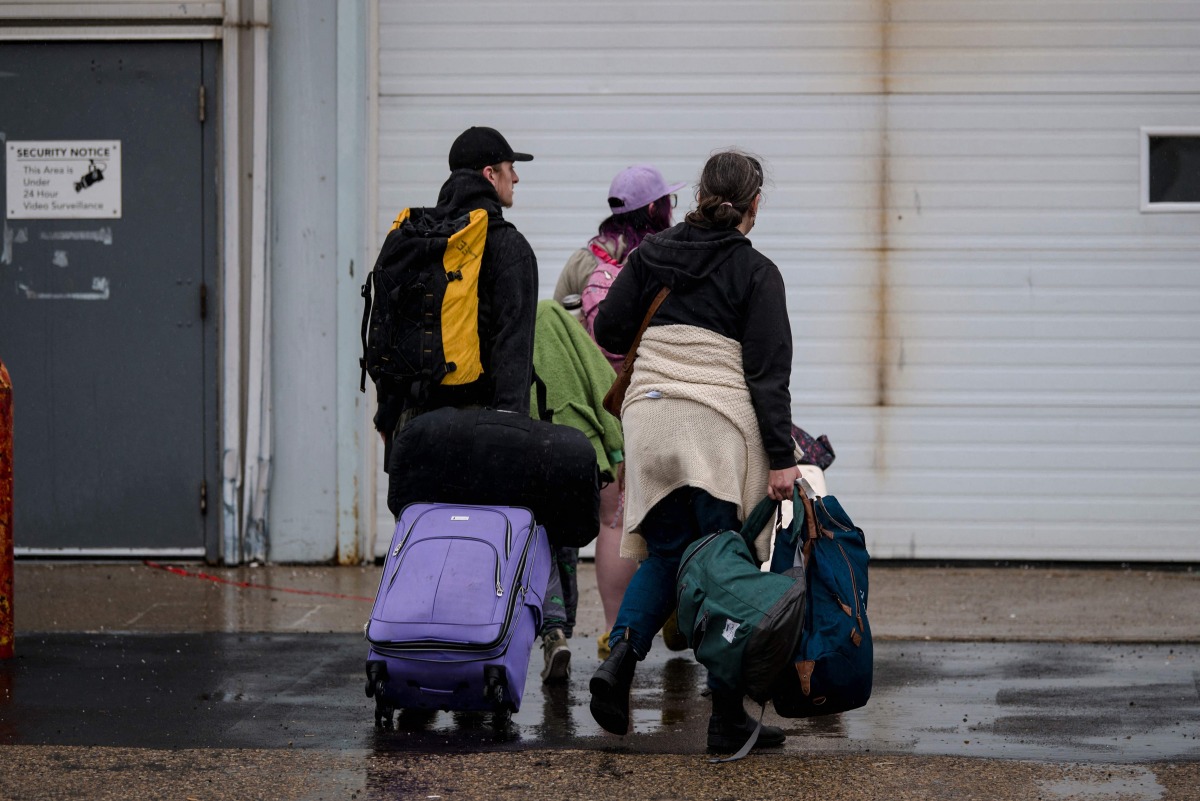 People carry bags near the Emergency response center at the Expo Center on August 18, 2023, in Edmonton, Canada. (Photo by ANDREJ IVANOV / AFP)
