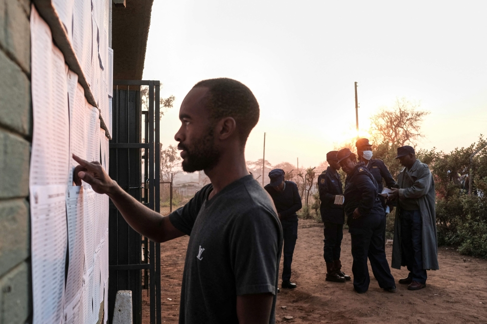 Zimbabwean police officers monitor a polling station as a man looks for his name on a voters list during Zimbabwe's presidential and legislative elections in Harare on August 23, 2023. (Photo by Jekesai NJIKIZANA / AFP)
