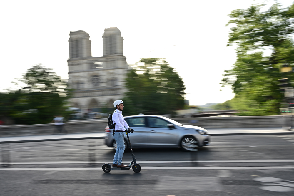A man rides his electric scooter or trottinette past the Notre-Dame de Paris Cathedral in Paris on August 23, 2023. (Photo by MIGUEL MEDINA / AFP)

